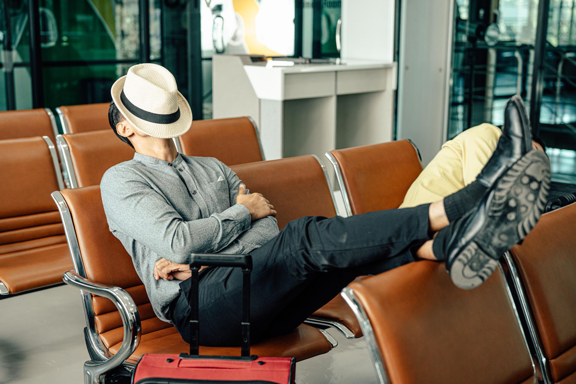 Young traveler man sleeping in airport while waiting airline flight to travel at airport terminal.